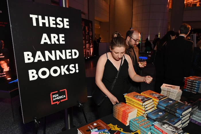 Des piles de livres posés sur une table avec des personnes autour.