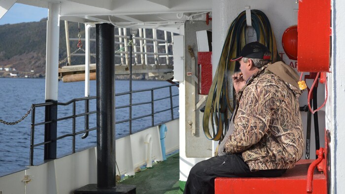 Un homme fume une cigarette sur le pont du traversier.
