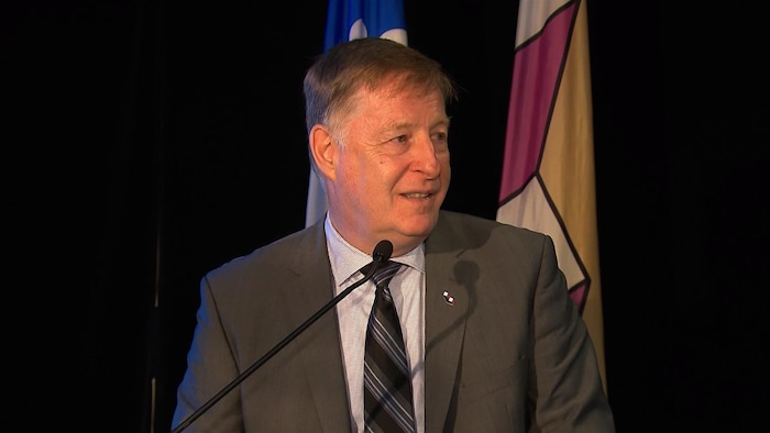 Le maire de Laval, Marc Demers, en conférence de presse, debout devant des drapeaux du Québec et de la Ville.