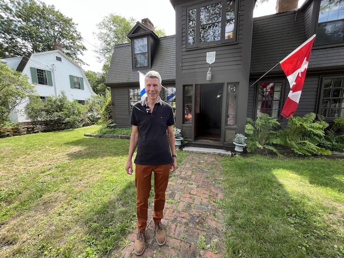 Un homme debout devant une vieille maison de bois.
