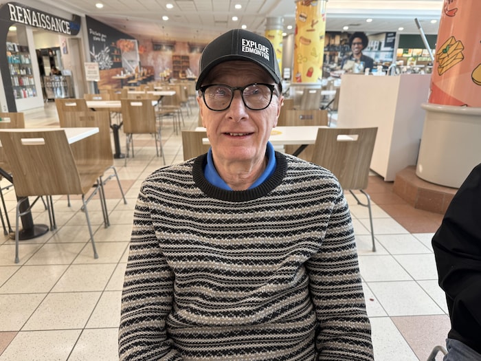 Un homme portant des lunettes et une casquette est attablé dans une aire de restauration du centre commercial Bonnie Doon, à Edmonton, en janvier 2026.