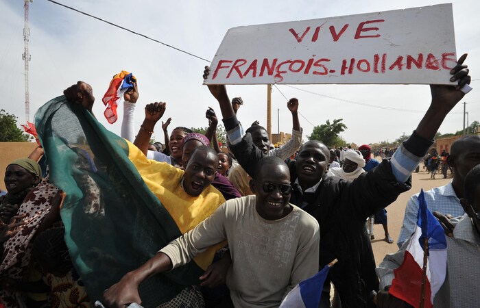 Des Maliens sourient et crient dans la rue. L'un d'eux tient une pancarte sur laquelle il est écrit : « Vive François Hollande ».