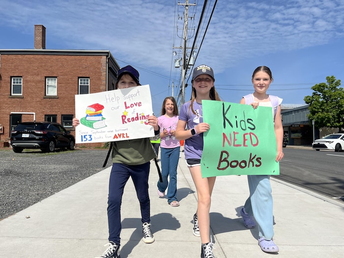 Des enfants avancent sur un trottoir avec des affiches «Les enfants ont besoin de livres» et «Aidez à soutenir notre amour pour la lecture».