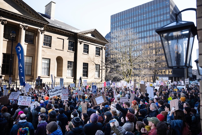 Une foule de plusieurs centaines de personnes, agitant des affiches, obstrue complètement une rue devant Province House.