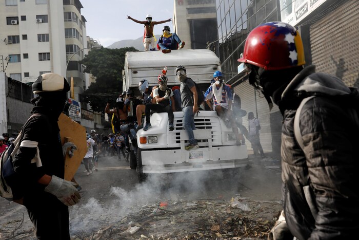 Des manifestants portant des masques à gaz et des casques sont montés sur un camion. Ils sont entourés d'une fumée blanche, qui est en fait du gaz.