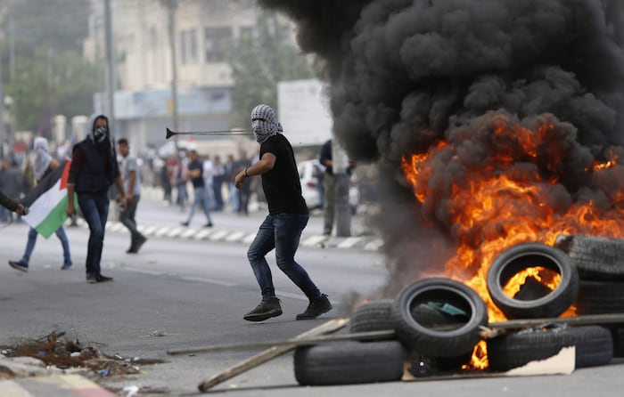 Un Palestinien masqué manie une fronde derrièere un barrage de pneus en feu.
