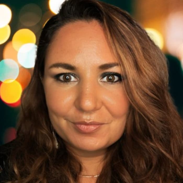 Une femme au visage souriant fixe du regard l'objectif d'une caméra.