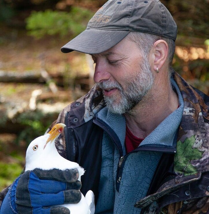 Mark Mallory dans la nature, coiffé d'une casquette et tenant un goéland dans ses bras.