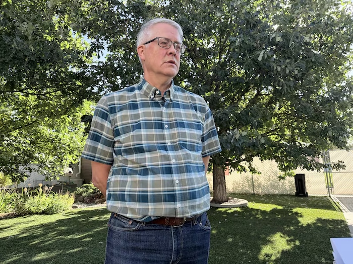 Un homme est debout dans un jardin, devant un arbre.