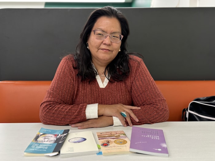 Une personne assise les bras croisés avec des livres disposés sur une table.
