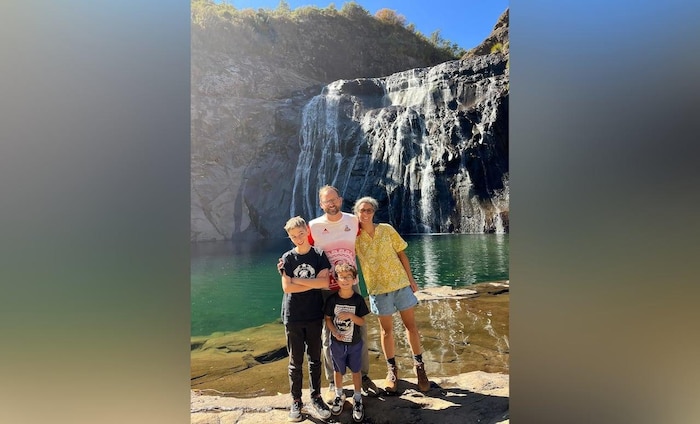 A man, a woman and their two children pose in front of a waterfall.