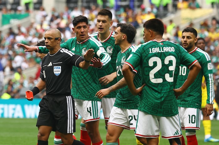 Un arbitre, carton rouge à la main, se tourne de dos à un groupe de joueurs en maillots verts.