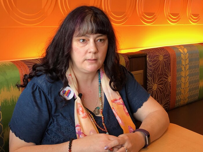 Une femme aux cheveux mauves et aux multiples bijoux fabriqués à la main explique avec ferveur sur les enjeux liés au trouble du spectre de l'autisme dans notre société.