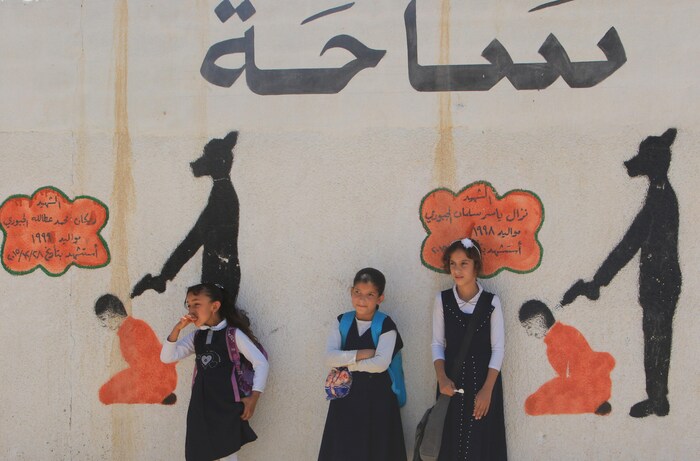 Des écolières attendent devant une murale représentant des djihadistes de l'EI en train d'exécuter des prisonniers.