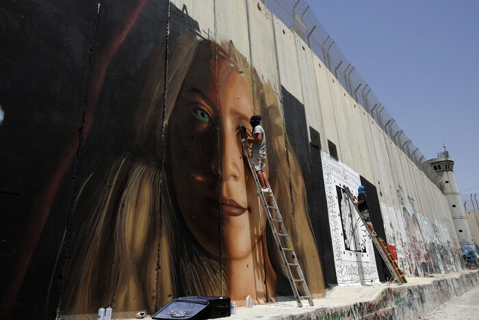 Italian artist Jorit Agoch (L) paints a mural depicting jailed Palestinian teenager Ahed Tamimi next to another artist on Israel's controversial separation barrier in the West Bank city of Bethlehem, on July 25,2018. - Tamimi, was charged earlier this year after a viral video showed her hitting two soldiers in the occupied West Bank. (Photo by Musa Al SHAER / AFP) / RESTRICTED TO EDITORIAL USE, MANDATORY MENTION OF THE ARTIST UPON PUBLICATION, TO ILLUSTRATE THE EVENT AS SPECIFIED IN THE CAPTION