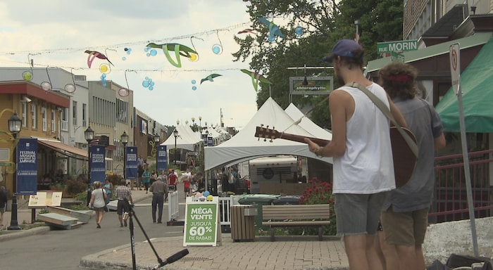 Deux musiciens, vus de dos, grattent la guitare devant une rue où circulent des dizaines de personnes sous des chapiteaux.