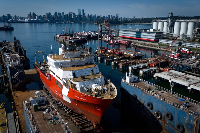 Photo aérienne d'un navire rouge et blanc, avec la ville de Vancouver en arrière-plan de l'autre côté de la rive.