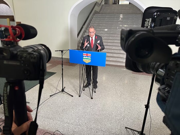 Le chef de l'opposition néo-démocrate de l'Alberta, Naheed Nenshi, se tient devant un microphone et le drapeau albertain.
