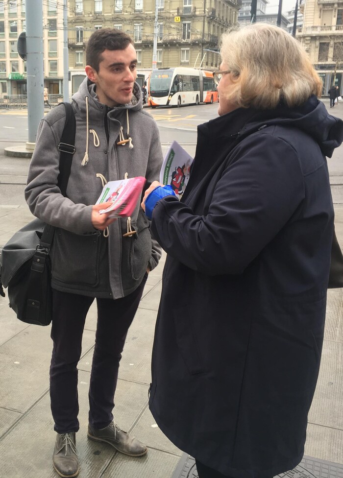 Un jeune homme distribue des tracts à une femme dans la rue à Genève.
