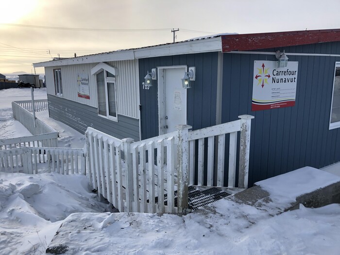 Façade d'un édifice en bois en hiver avec des escaliers qui descendent vers la porte d'entrée.
