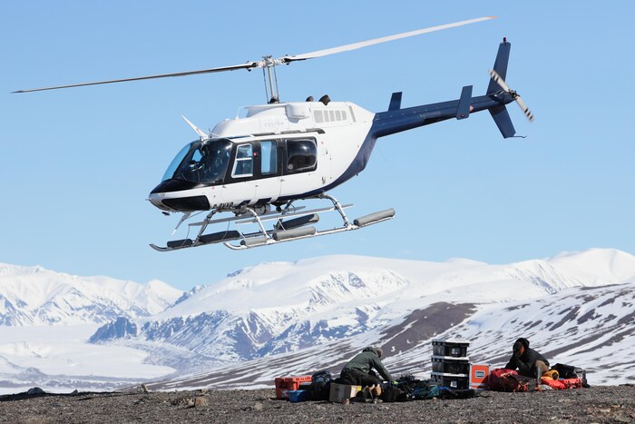 Un hélicoptère dans les airs au-dessus de deux chercheurs qui rangent leur équipement, sur l'île Bylot, au Nunavut, le 17 juin 2022.