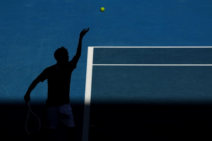 La silhouette du joueur de tennis, qui vient de lancer la balle en l'air avant de la frapper avec sa raquette.