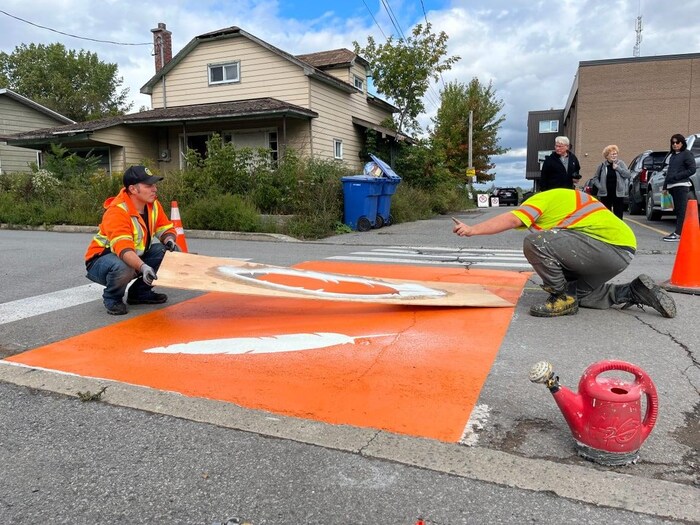 Workers stencil eagle feathers onto a freshly painted crosswalk outside of Kateri School in Kahnawake, south of Montreal on Wednesday. 