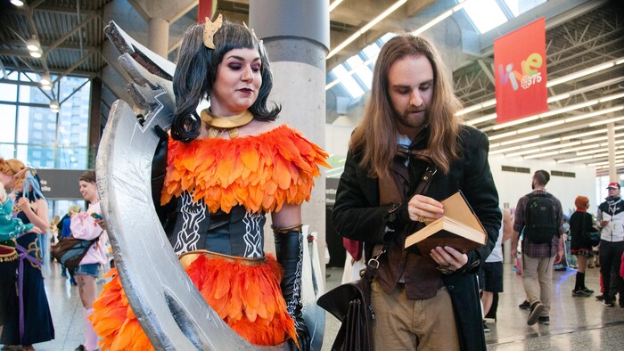 Une femme déguisé en personnage de jeux vidéo regarde son ami ajuster un de ses accessoires.