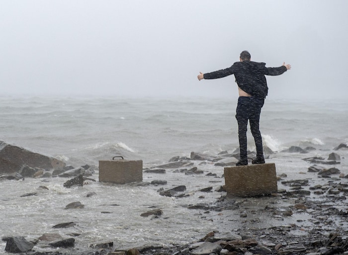 Un homme debout sur un morceau de béton fait face à l'océan et aux vents violents.