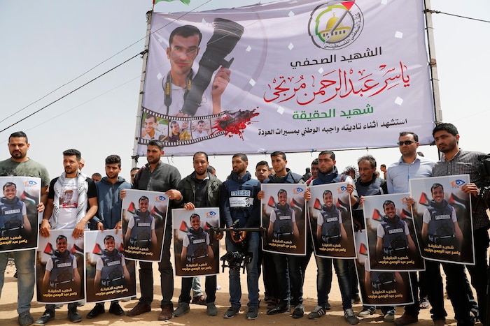 Une dizaine d'hommes tiennent des affiches montrant Yasser Murtaja. Au milieu du groupe, un homme porte une caméra et une veste pare-balles sur laquelle on lire « Presse ».