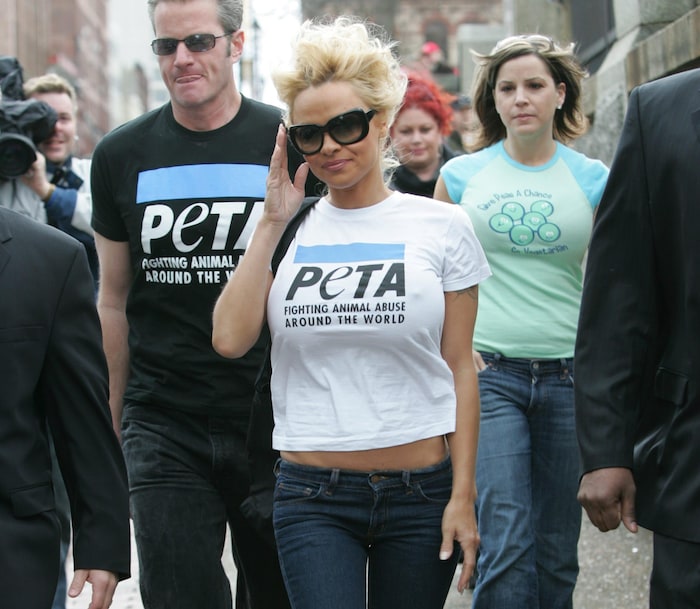 Pamela Anderson walks down the street.  She's wearing a PETA t-shirt and adjusting her sunglasses.
