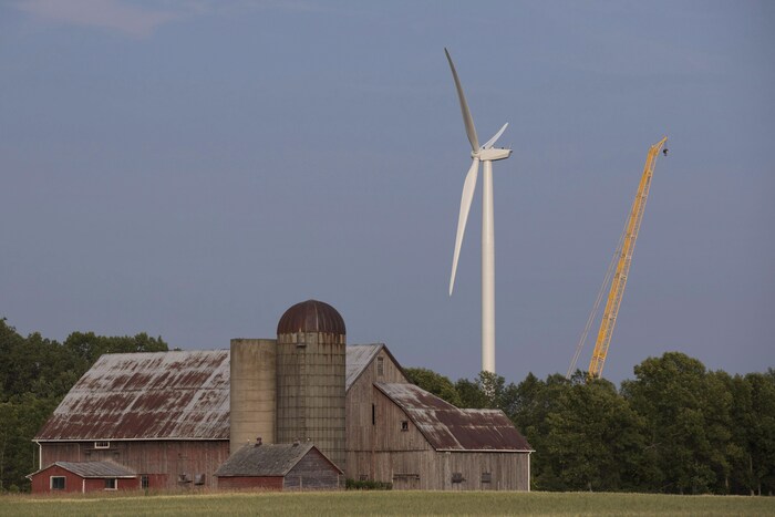 Une éolienne et une grue derrière une grange.