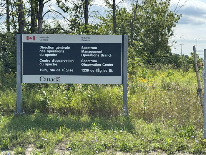 Un panneau gouvernemental bilingue se dresse au milieu d’une végétation dense, en bordure d’un chemin.