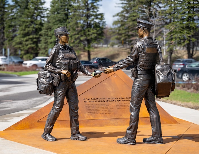 Deux statues de policiers en uniforme se font face et tiennent ensemble un sablier au-dessus d'un socle triangulaire.