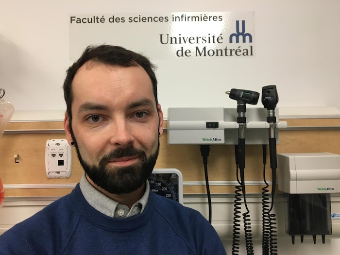 On voit M. Lavoie qui sourit à la caméra. Derrière lui se trouvent des instruments médicaux et une affichette de la Faculté des sciences infirmières de l'Université de Montréal.