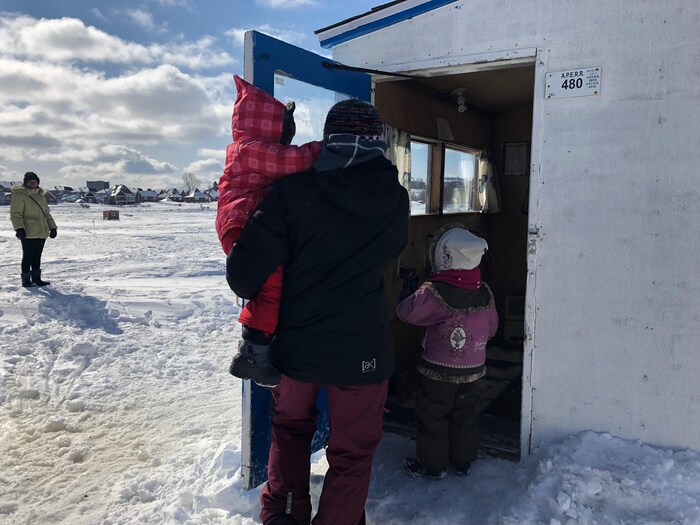 Une mère et ses deux petites filles entrent dans une cabane de pêche.