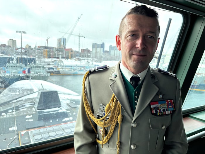 Le colonel en uniforme est photographié à l'intérieur de la frégate. Derrière lui se trouvent le port d'Halifax enneigé et de nombreuses grues de construction.