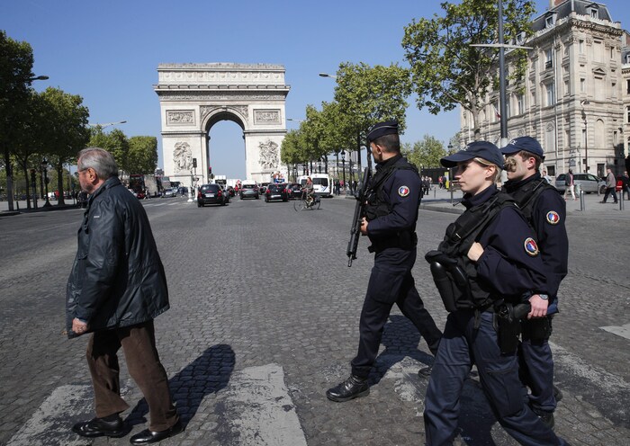 Trois policiers français armés traversent les Champs-Élysées. 