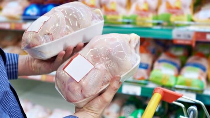 Un consommateur tient deux poulets emballés dans une épicerie.