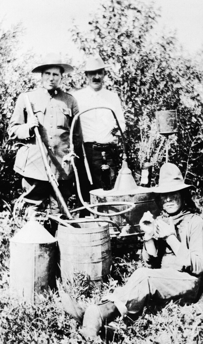 Trois personnes posent à côté d'un alambic illégal près de Cardston, au début des années 1920. 
