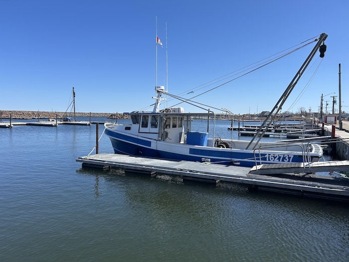 Un bateau bleu et blanc amarré dans un quai. Au loin, on voit un gros mur de roches qui entoure le quai.