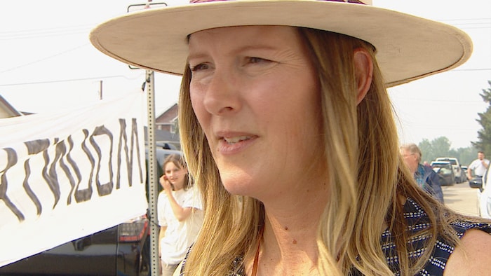 Une femme se couvre la tête avec un large chapeau lors d'une manifestation à Fort MacLeod, en Alberta, contre l'industrie charbonnière, le 11 juin 2025.