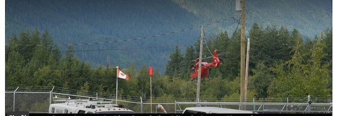 Un hélicoptère rouge survvole une zone forestière, à Squamish, en Colombie-Britannique.