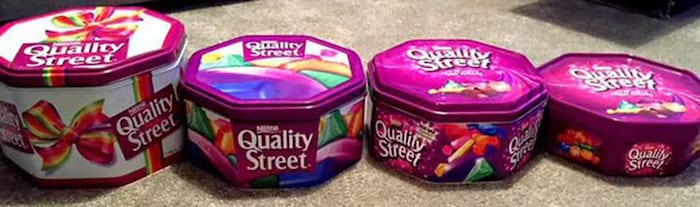 Des boîtes métalliques remplies de chocolats Quality Street placées côte à côte pour en comparer la taille.
