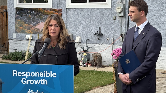 Danielle Smith devant un lutrin en compagnie de Dan Williams dans une cour arrière de maison.