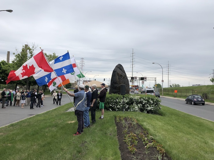 Des hommes brandissent, près de la Roche noire, des drapeaux canadien, québécois, montréalais et irlandais.