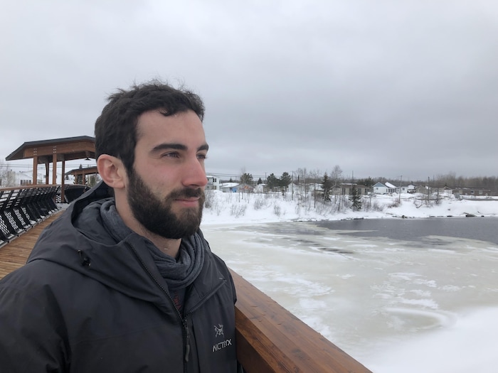 Rodrigue Turgeon, portant un manteau noir, regarde vers la rivière sous un ciel nuageux et sombre.