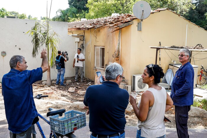 Quatre Israéliens sont rassemblés près d'une maison touchée par une roquette. Le toit est en partie détruit. Une équipe de la télévision israélienne est au travail devant la maison.