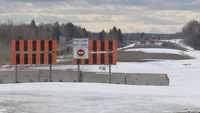 Une voie de circulation inachevée et barrée par des blocs de béton et des panneaux indicateurs.