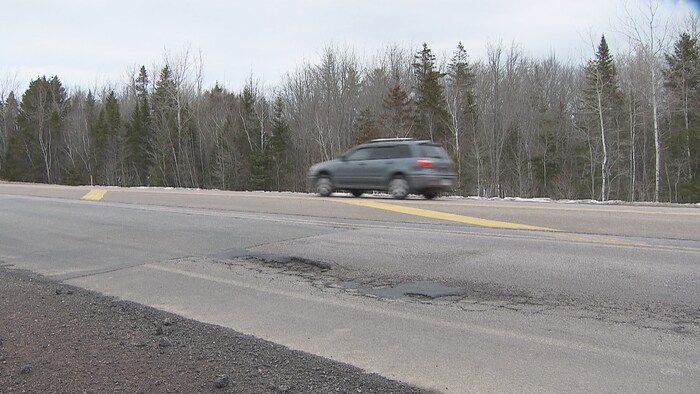 Une voiture circule à côté du trou dans la chaussée.